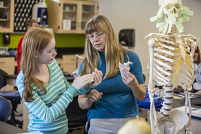 Professor talks to student in science lab with skeleton in foreground