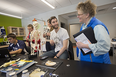 Professor standing in computer lab smiling at students with skeleton in background