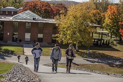 Three students walk up hill on campus with fall foliage and library behind them