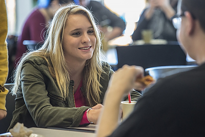 Student smiles at another student in dining hall