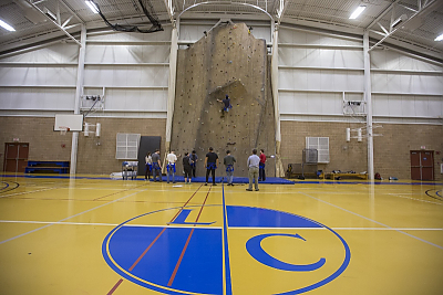 Students stand in front of climbing wall in Click Center gym with LC logo on floor in foreground