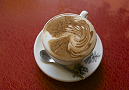 Latte with swirled pattern on top, served in cup atop saucer with pinecone pattern.