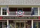 Front of store reading PUTNEY GENERAL STORE & PHARMACY. Red, white, and blue bunting and flags on front.