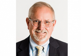 Headshot of Dr. James Dlugos, short gray hair and glasses, wearing dark suit jacket with yellow and blue patterned neck tie